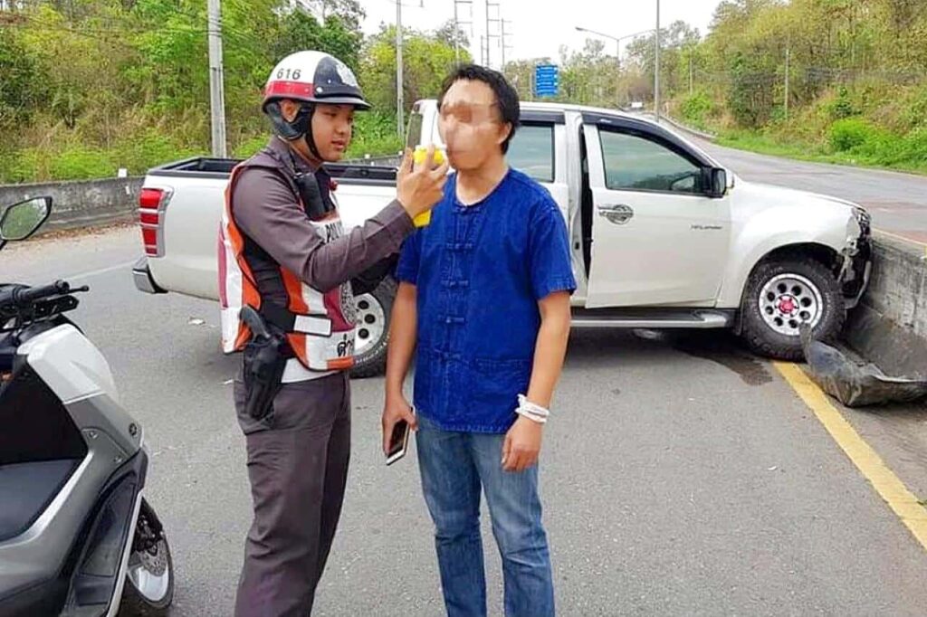 A police officer conducts a breathalyzer test on a driver after a road accident in Thailand
