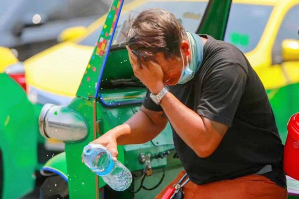 Un conducteur de tuk tuk se rafraichit le visage avec de l'eau