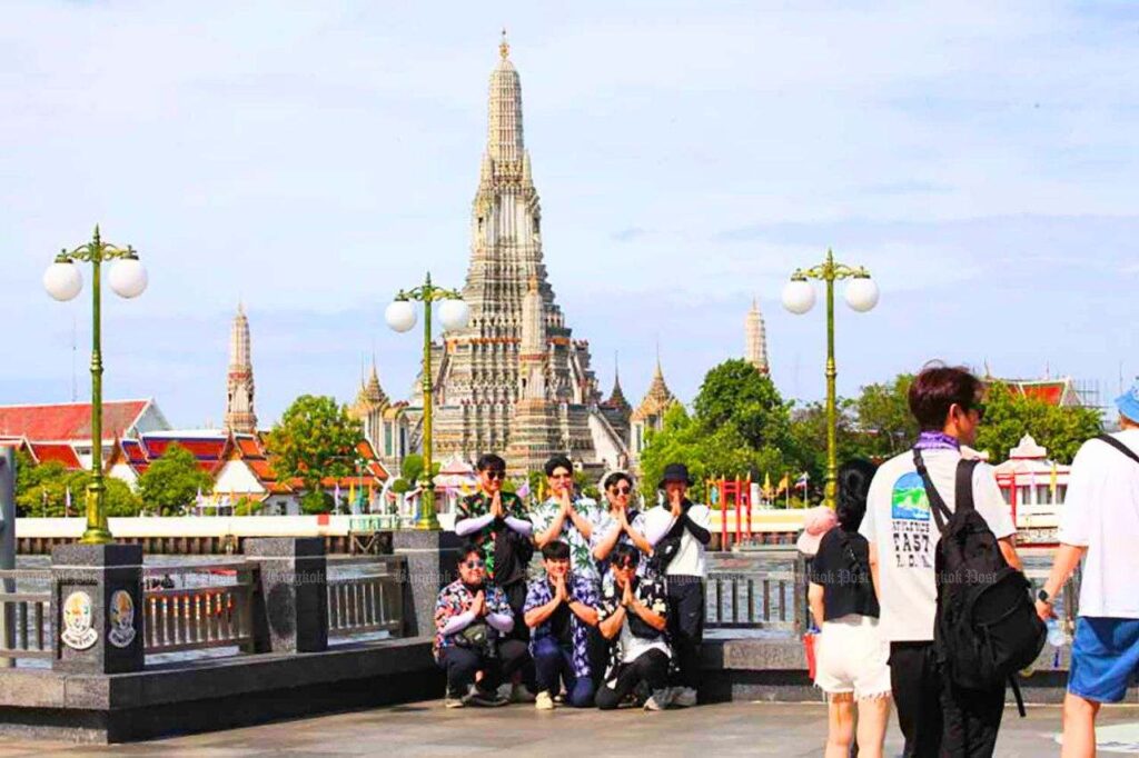Des touristes posent pour des photos à l'embarcadère de Tha Tien, au bord du fleuve Chao Phraya, en face du temple de l'Aube (Wat Arun) à Bangkok