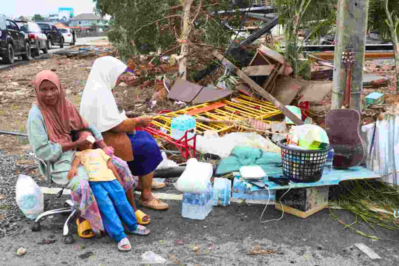 Une femme donne du lait à sa fille tandis qu'elle et une autre femme attendent devant leur maison endommagée par les inondations dans la commune de Khuan Lang, dans le district de Hat Yai, à Songkhla, avec leurs effets personnels