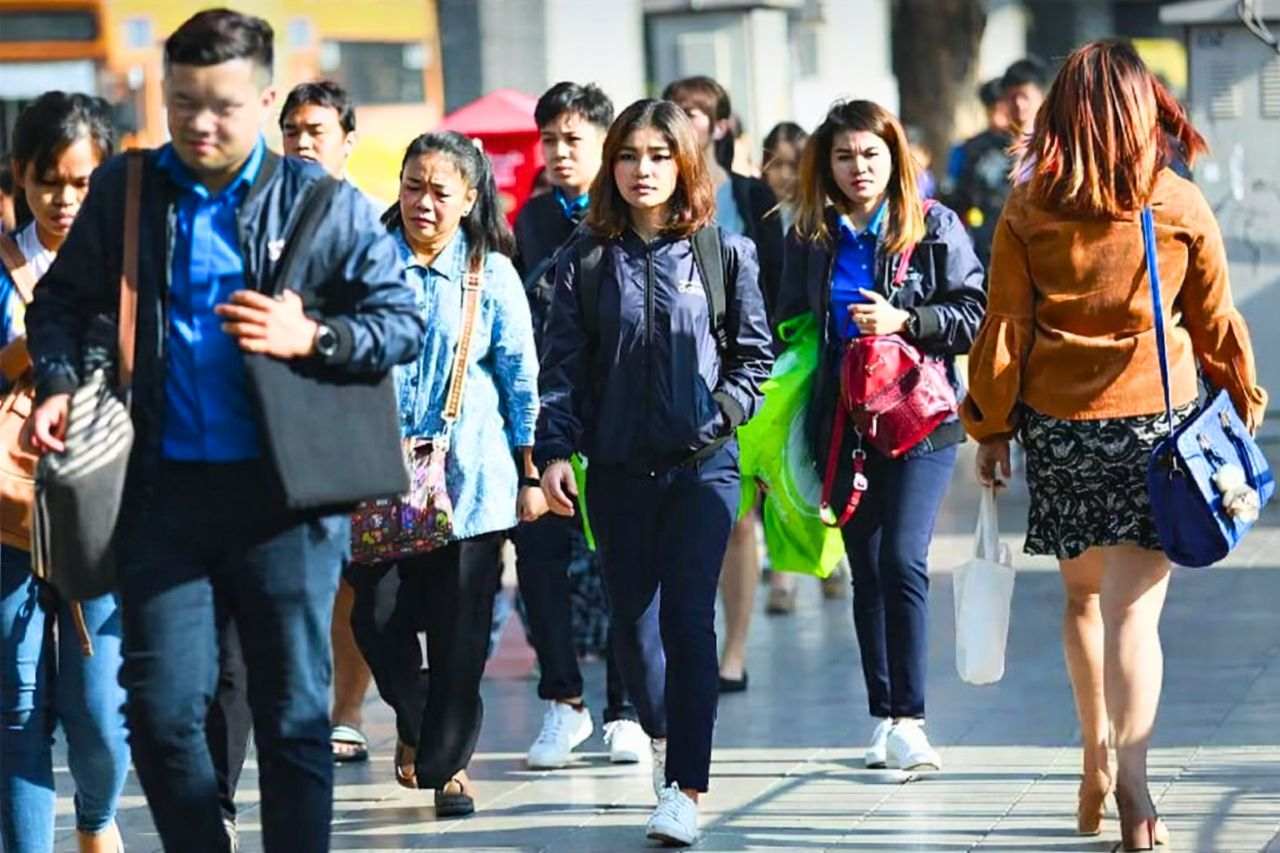 Des passants marchent dans une rue de Bangkok par temps frais, portant des vestes légères