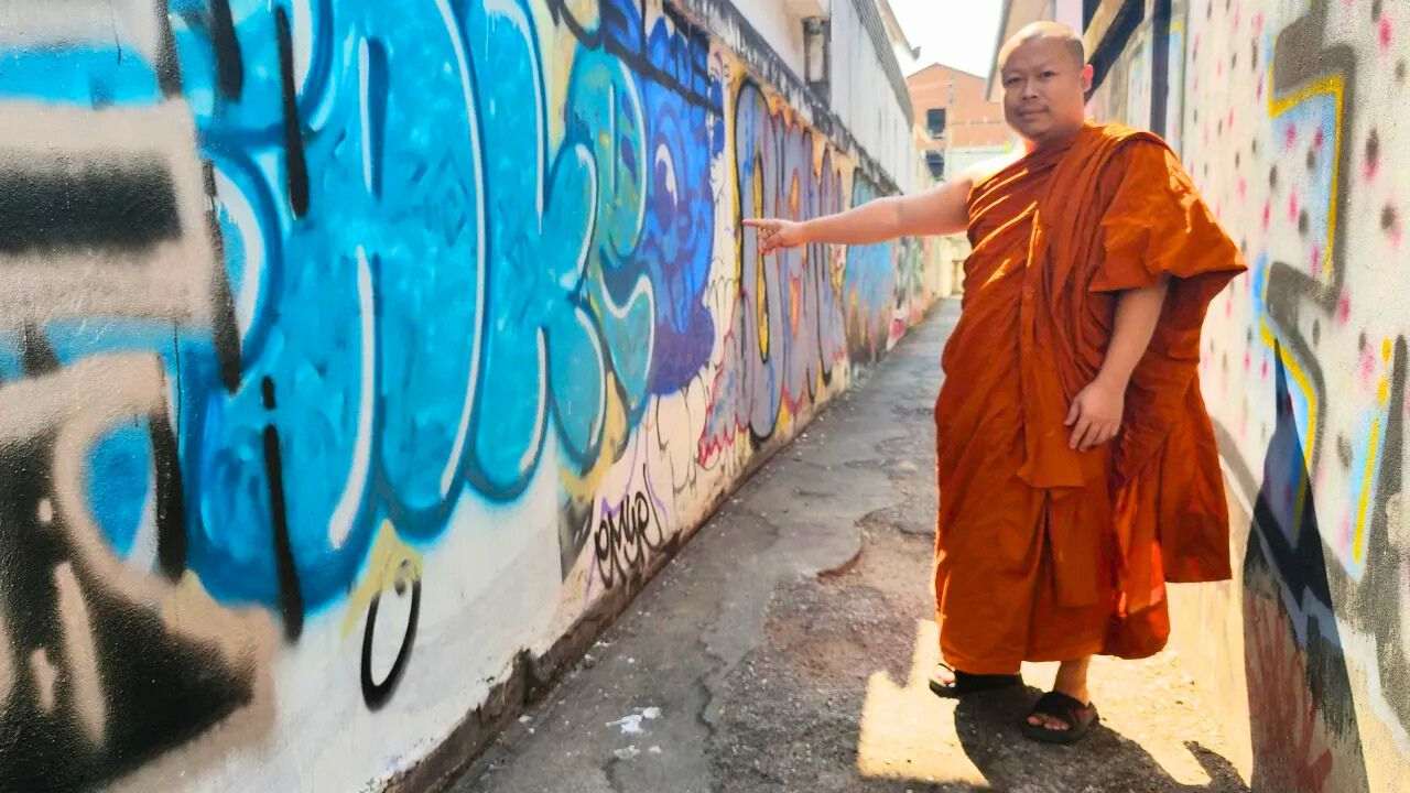 A monk points out the graffiti on the wall of Wat Dok Euang temple in Chiang Mai