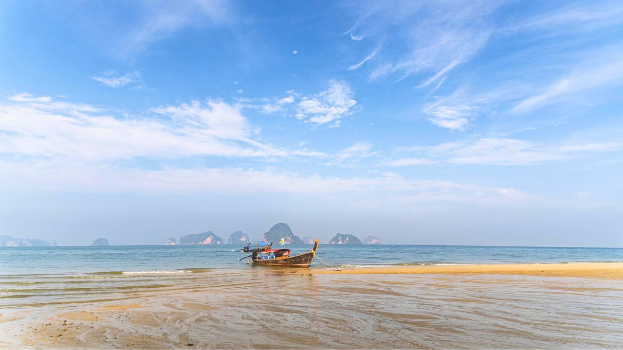 Un bateau à longue queue thaïlandais traditionnel sur une plage tropicale paisible, avec en arrière-plan le lagon bleu de l'île de Hong, à Krabi, en Thaïlande