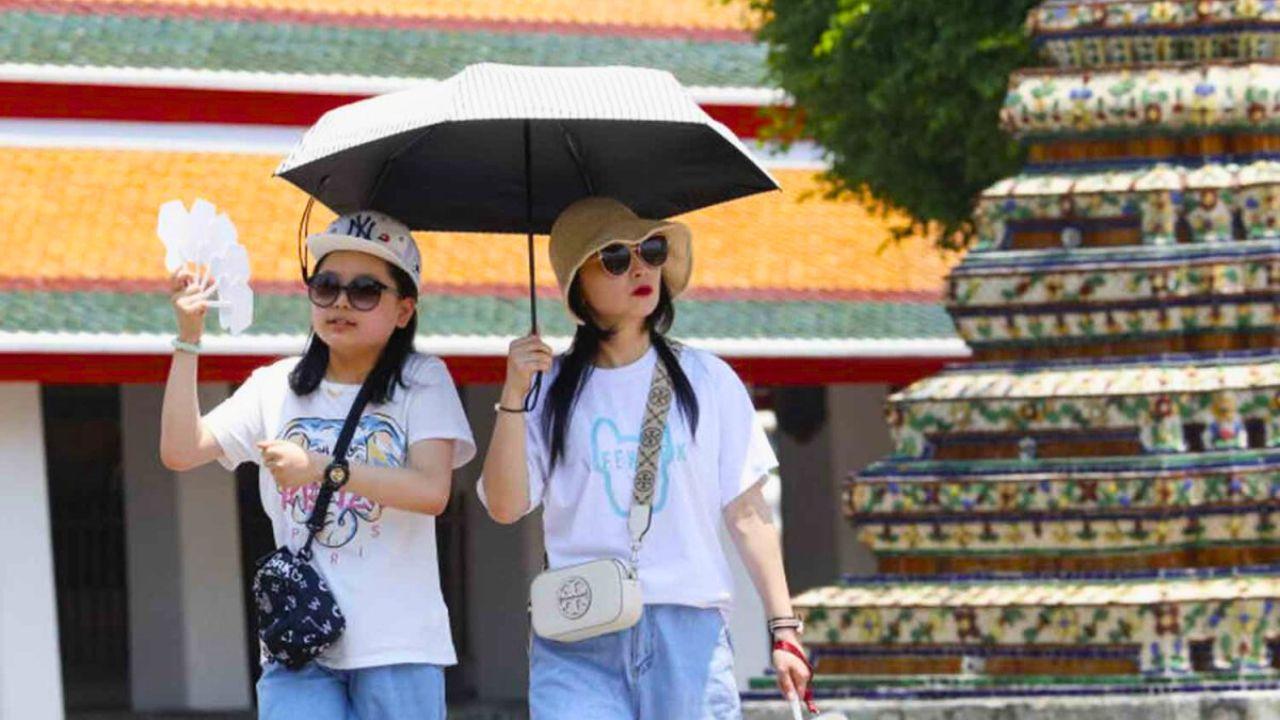Touristes se protégeant du soleil avec un parapluie et un éventail devant un temple en Thaïlande pendant une forte chaleur