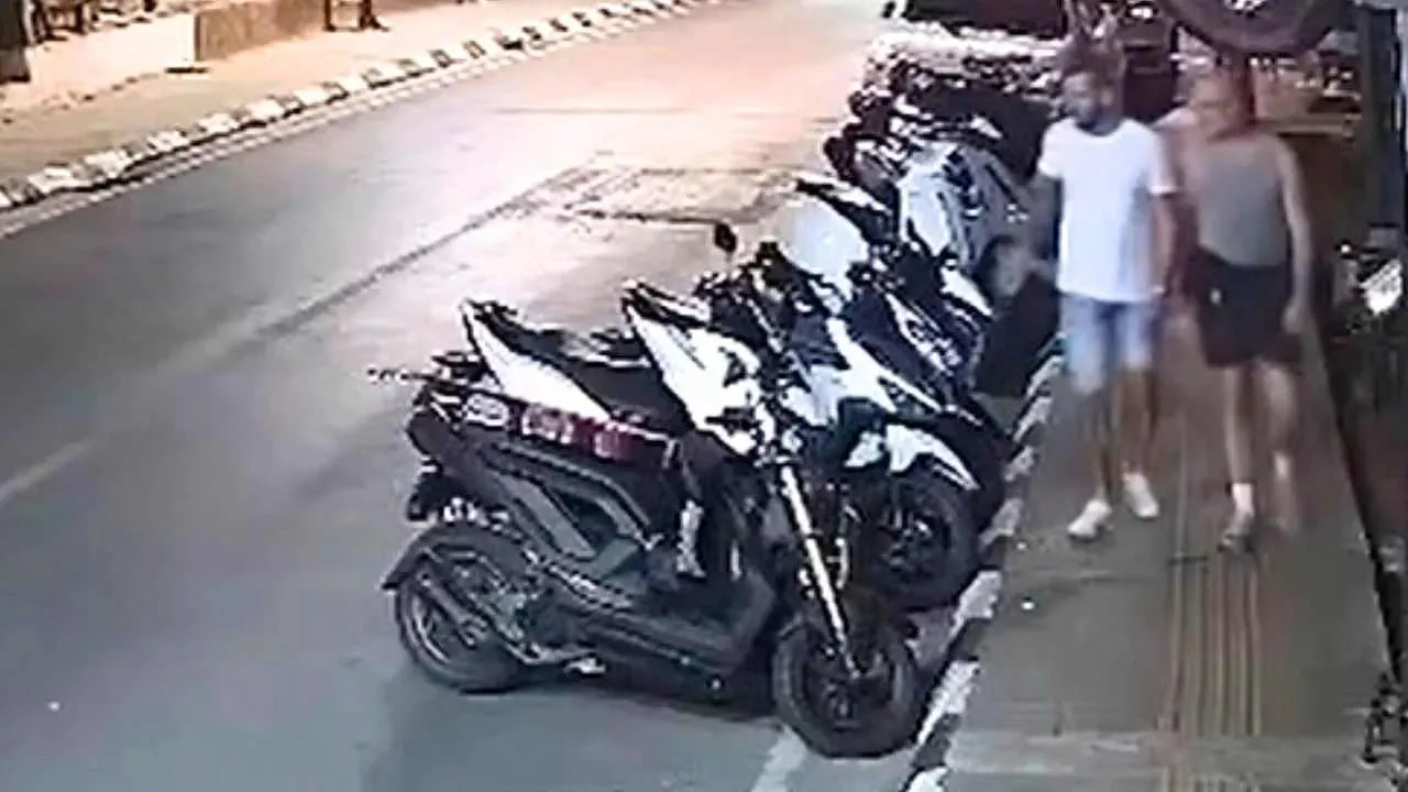 Deux hommes marchent près de motos stationnées sur un trottoir à Phuket, filmés par une caméra de surveillance