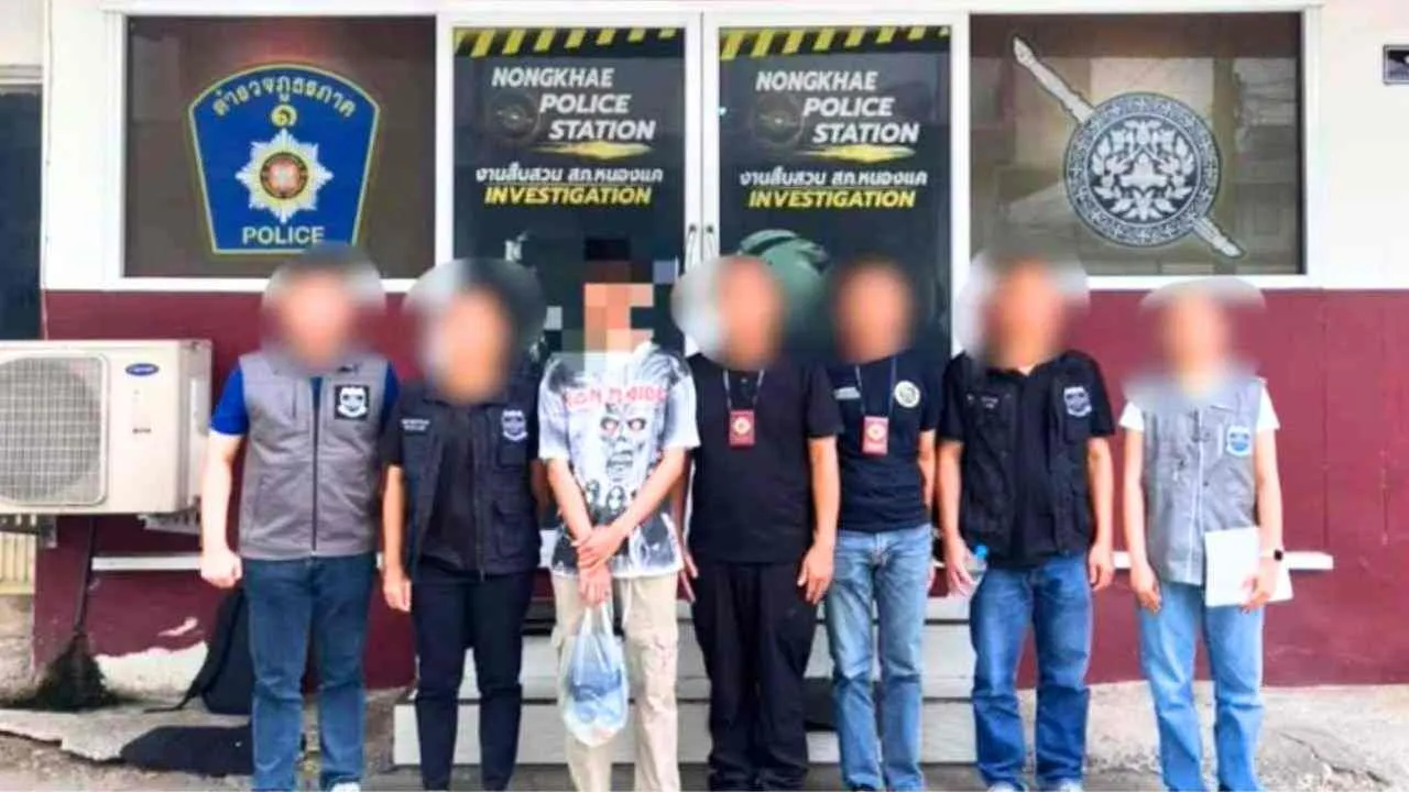 Le suspect arrêté dans l’affaire d’arnaque aux réservations d’hôtel entouré d’enquêteurs devant un commissariat en Thaïlande
