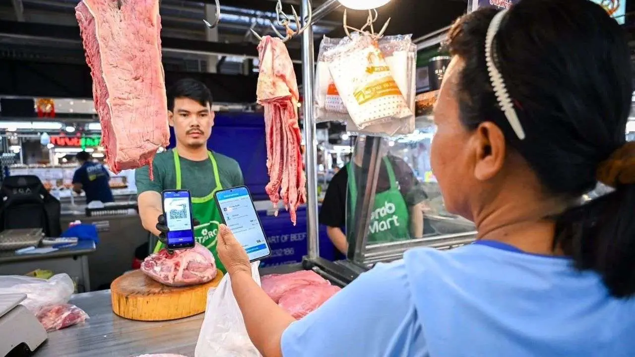 Une cliente règle ses achats dans une boucherie de marché grâce à l'application du programme « Thais Help Thais Plus : 60/40 ».