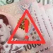 Billets de baht thaïlandais devant des dollars américains avec un symbole d'alerte sur fond de préoccupations économiques