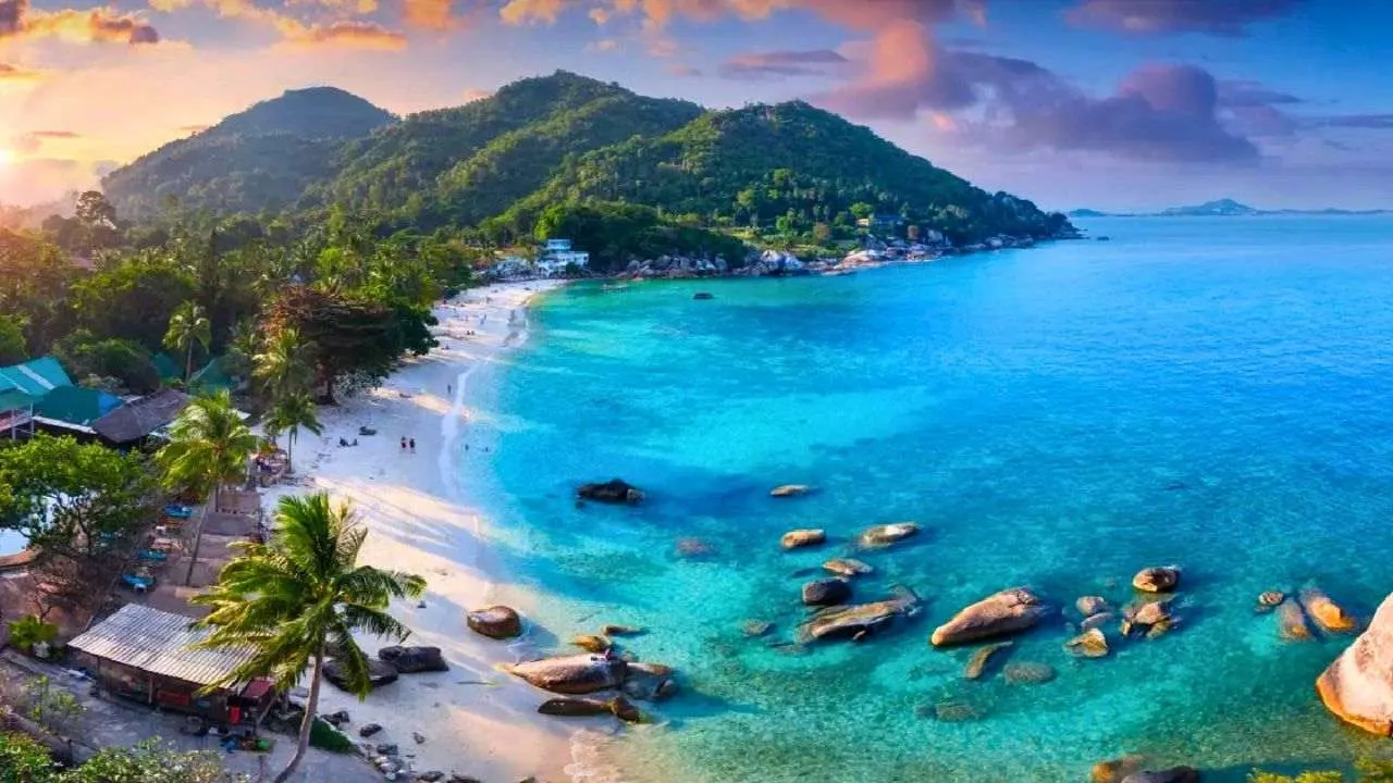 Vue aérienne d'une plage de Koh Samui aux eaux turquoise bordée de palmiers et de collines tropicales en Thaïlande