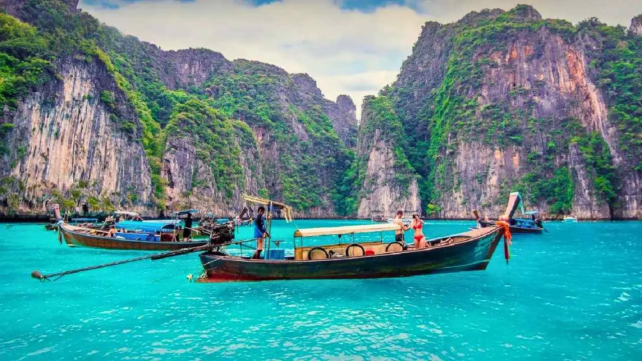 Bateau traditionnel long-tail naviguant dans les eaux turquoise entourées de falaises calcaires dans le sud de la Thaïlande.