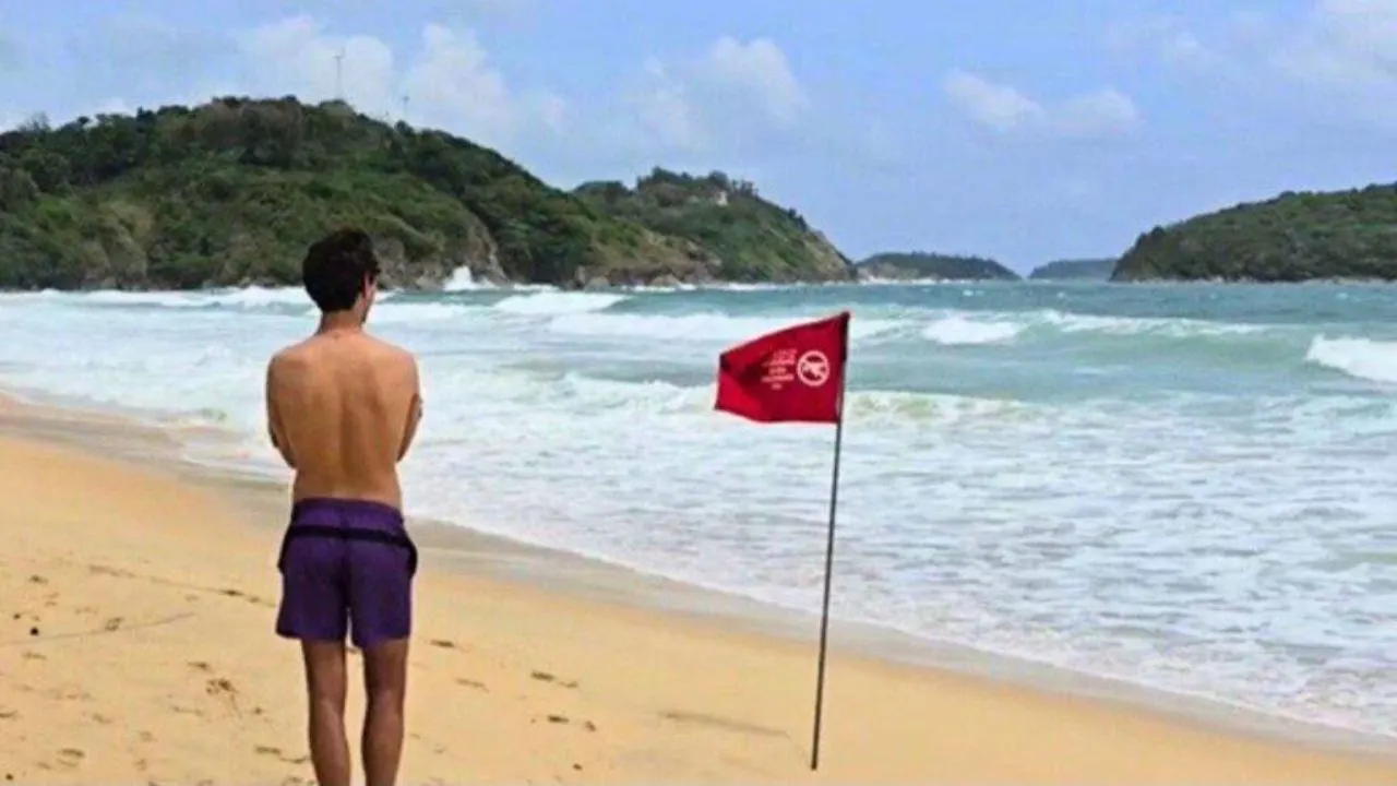 Un touriste regarde la mer agitée alors que des drapeaux rouges interdisent les baignades sur la plage de Nai Harn à Phuket