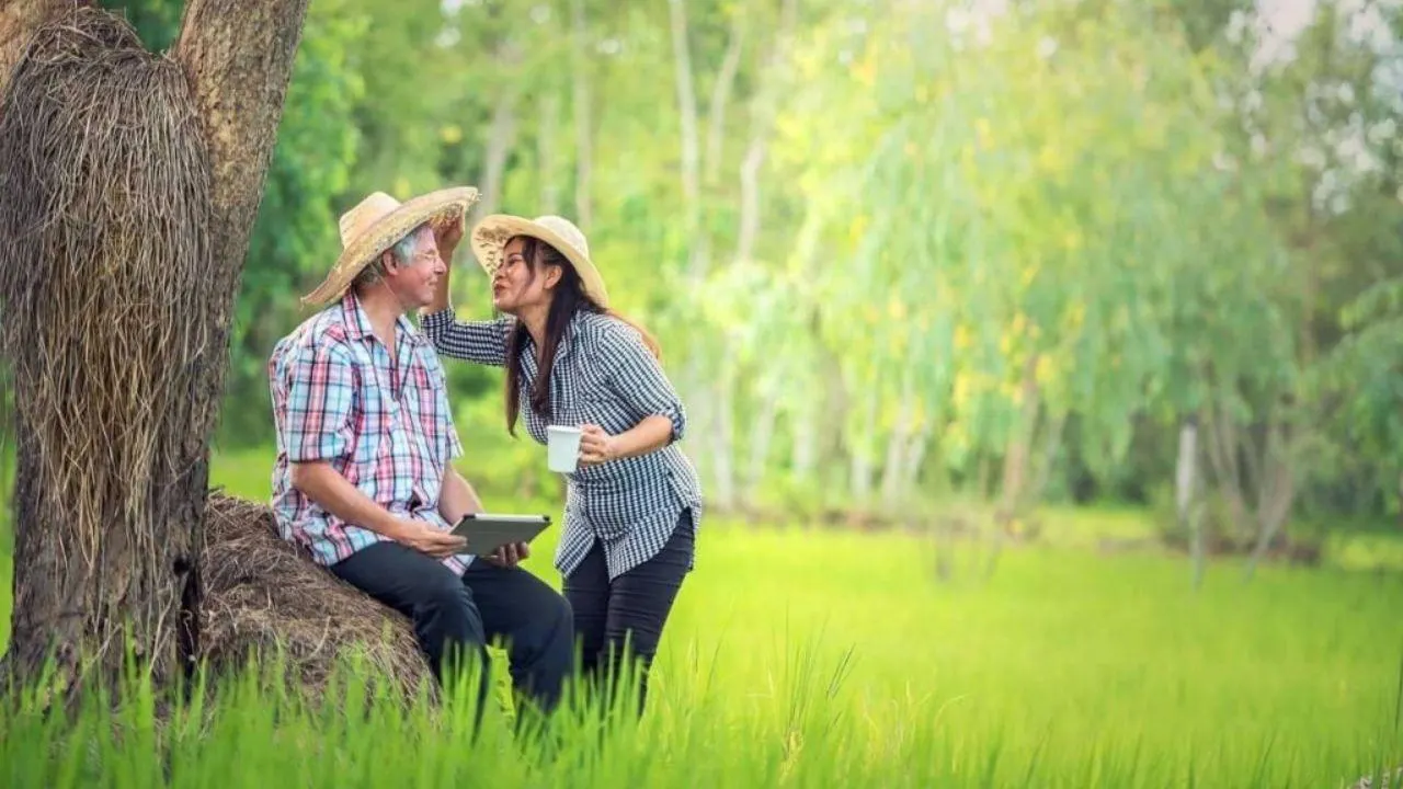 Un homme occidental et une femme thaïlandaise dans la campagne thaïlandaise, assis sous un arbre au bord d'un champ verdoyant